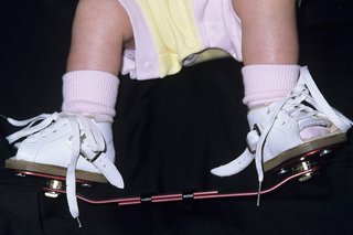 Stopy dziecka z butami przyczepionymi do drążka